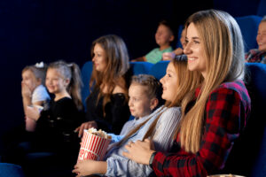 "Mama z dwójką dzieci siedzących na fotelach w kinie Bajka w Błoniu, wszyscy uśmiechnięci i skupieni na ekranie